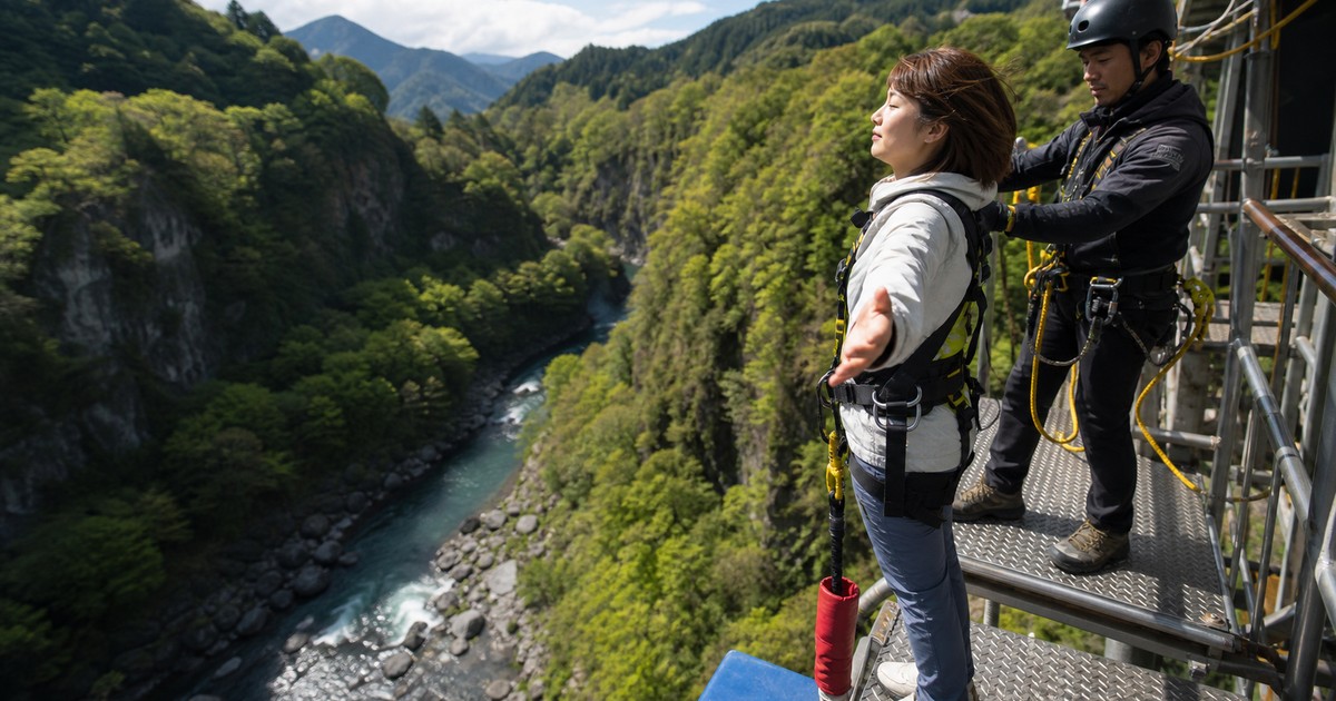 洋服姿の女性が山の渓谷にあるバンジー台で安全確認を受ける利用イメージ