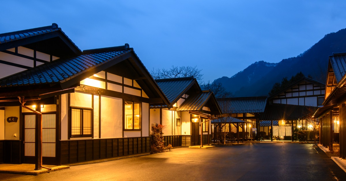 夕暮れの山並みと灯りがともる猿ヶ京温泉の旅籠屋丸一