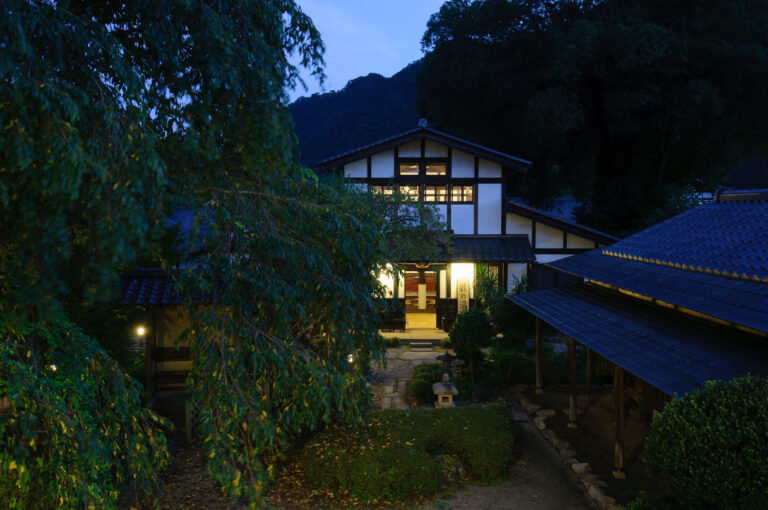 9月の夕暮れに灯りがともる旅籠屋丸一の庭と建物