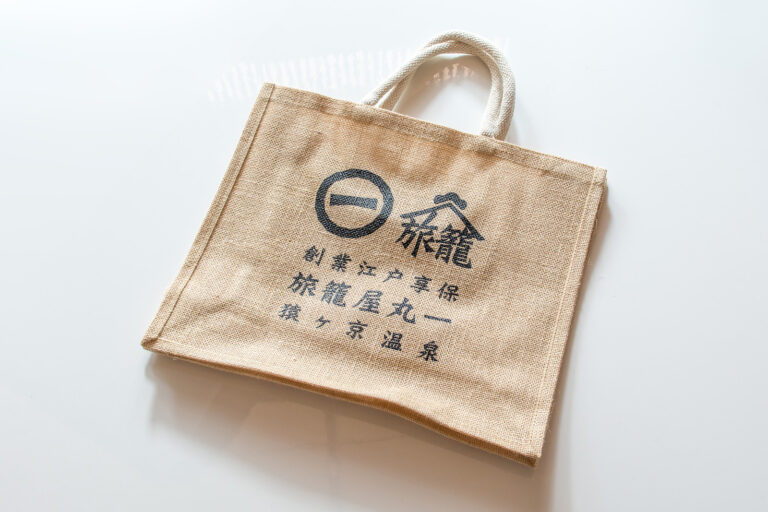 丸一印と旅籠屋丸一の文字を配した生成り色のバッグ