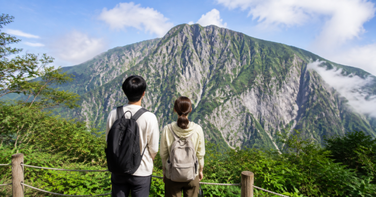 谷川岳の大きな岩壁を安全な場所から眺める旅行中のカップルの利用イメージ