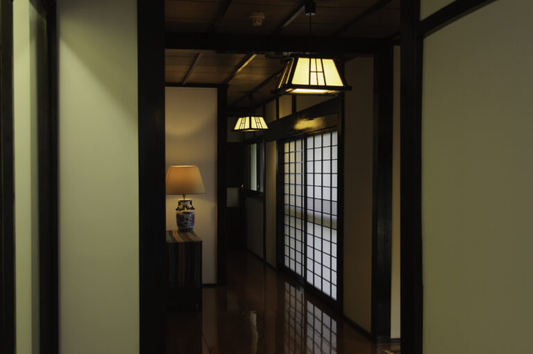 黒い木の柱と白壁、障子、行灯が続く旅籠屋丸一の本館廊下