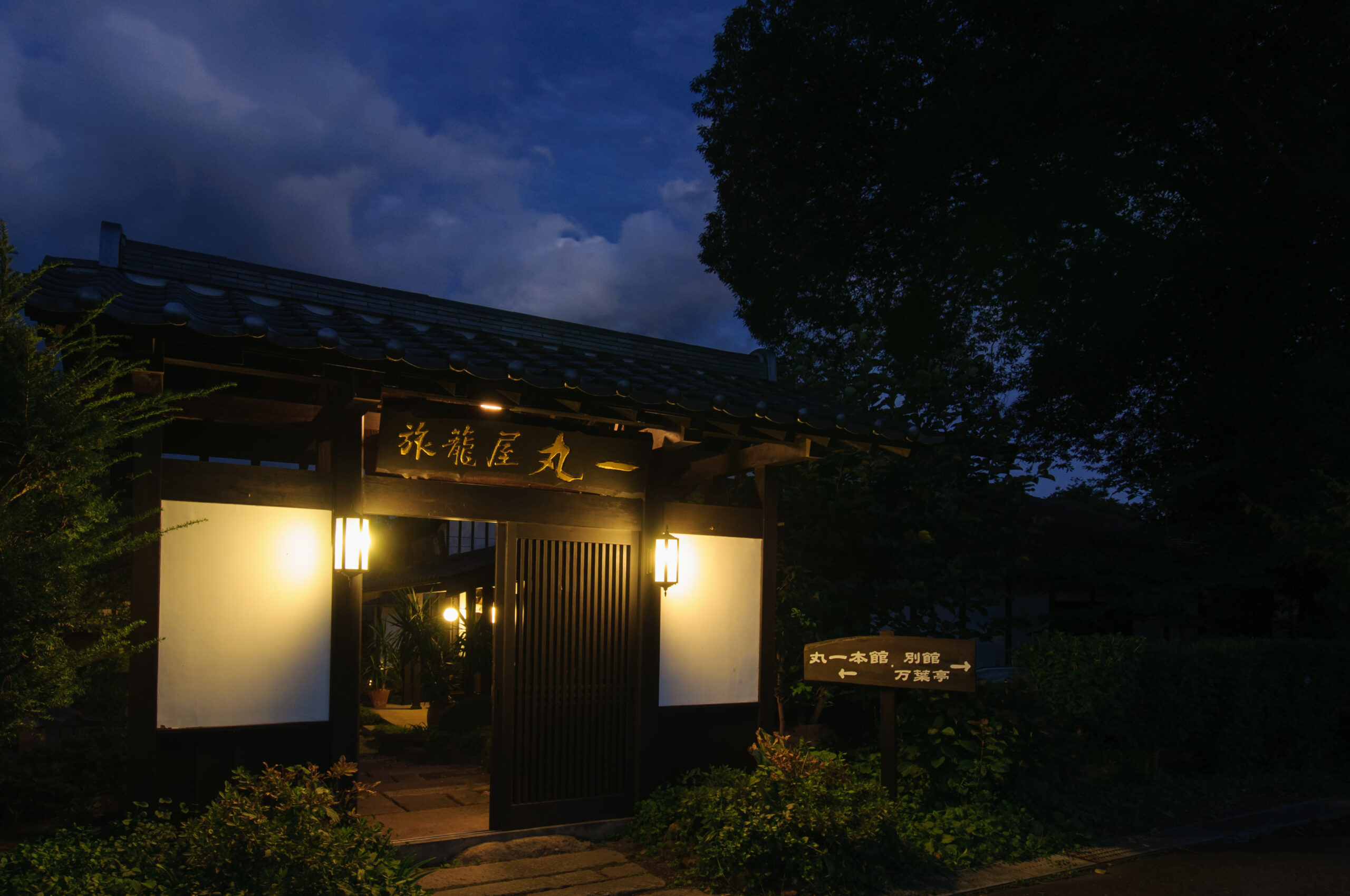 夜の青い空と灯りに包まれた旅籠屋丸一の門