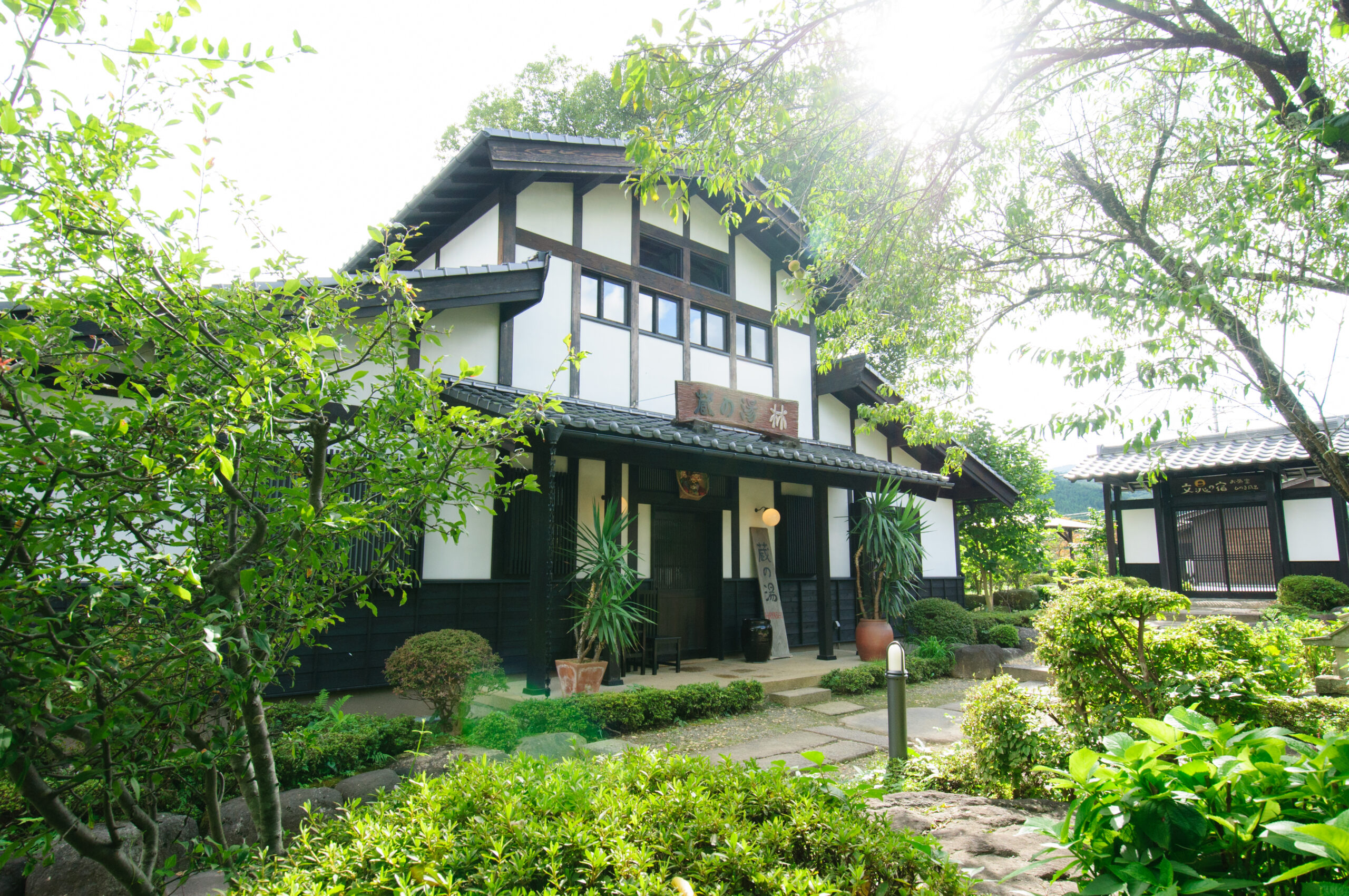 昼の光に包まれた旅籠屋丸一の庭木と蔵の湯